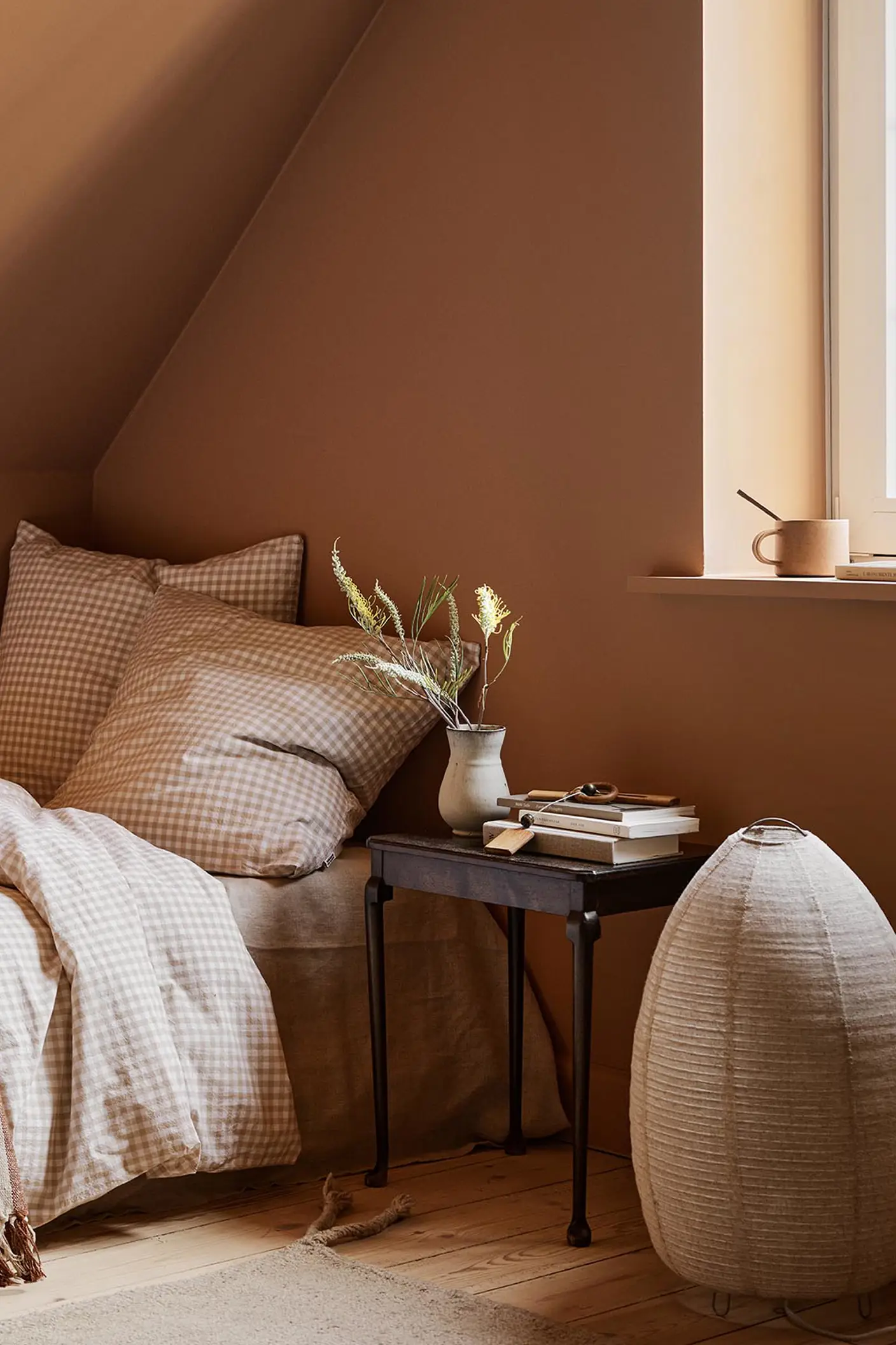 Bedroom with checkered bedding and a black side table against a ochre coloured wall painted with 11220 Ochre Clay from Jotun.