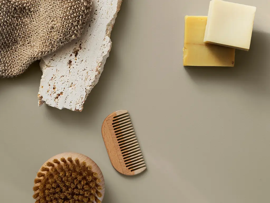 Naturliga hudvårdsprodukter, inklusive en exfolierande tvättvante, träkam, tvålar och borste, placerade på en ljus yta.