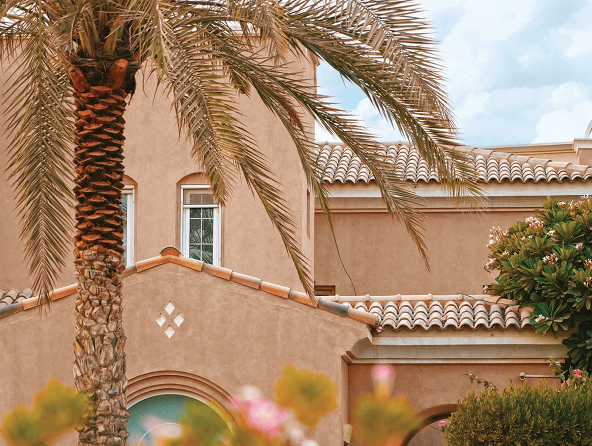 Mediterranean-style house with terracotta roof tiles, surrounded by palm trees and lush greenery