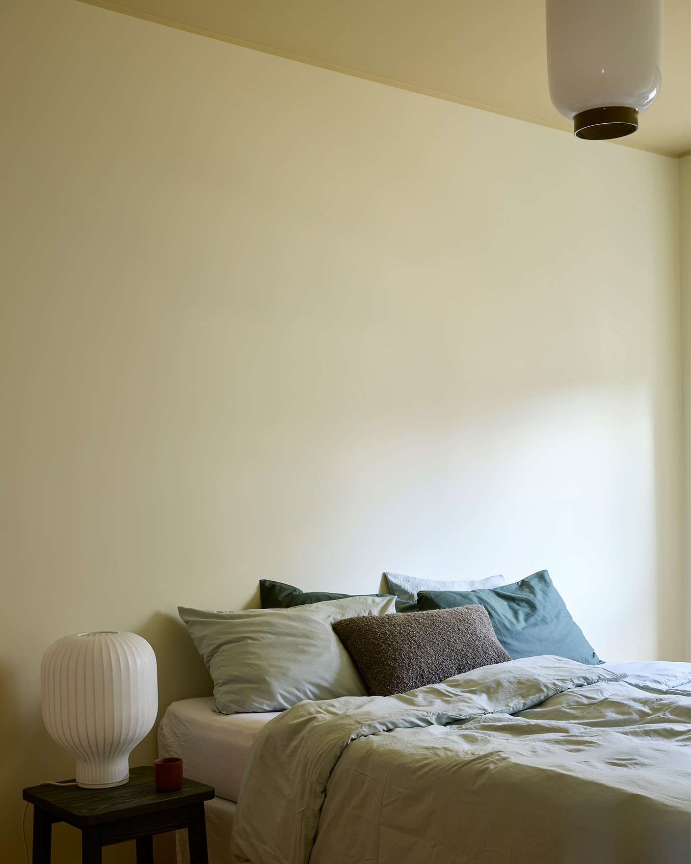 Et gult soverom malt i fargen Jotun Malmø, og taket er malt i Earthy Yellow. Ved siden av sengen står et nattbord med en lampe. 