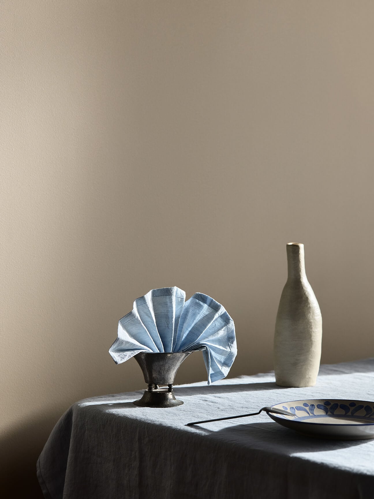 Et spisebord med blå og klare glasskanner foran beige vegger malt i Jotun 10966 Almond Beige