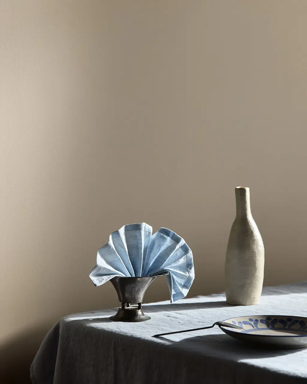Et spisebord med blå og klare glasskanner foran beige vegger malt i Jotun 10966 Almond Beige