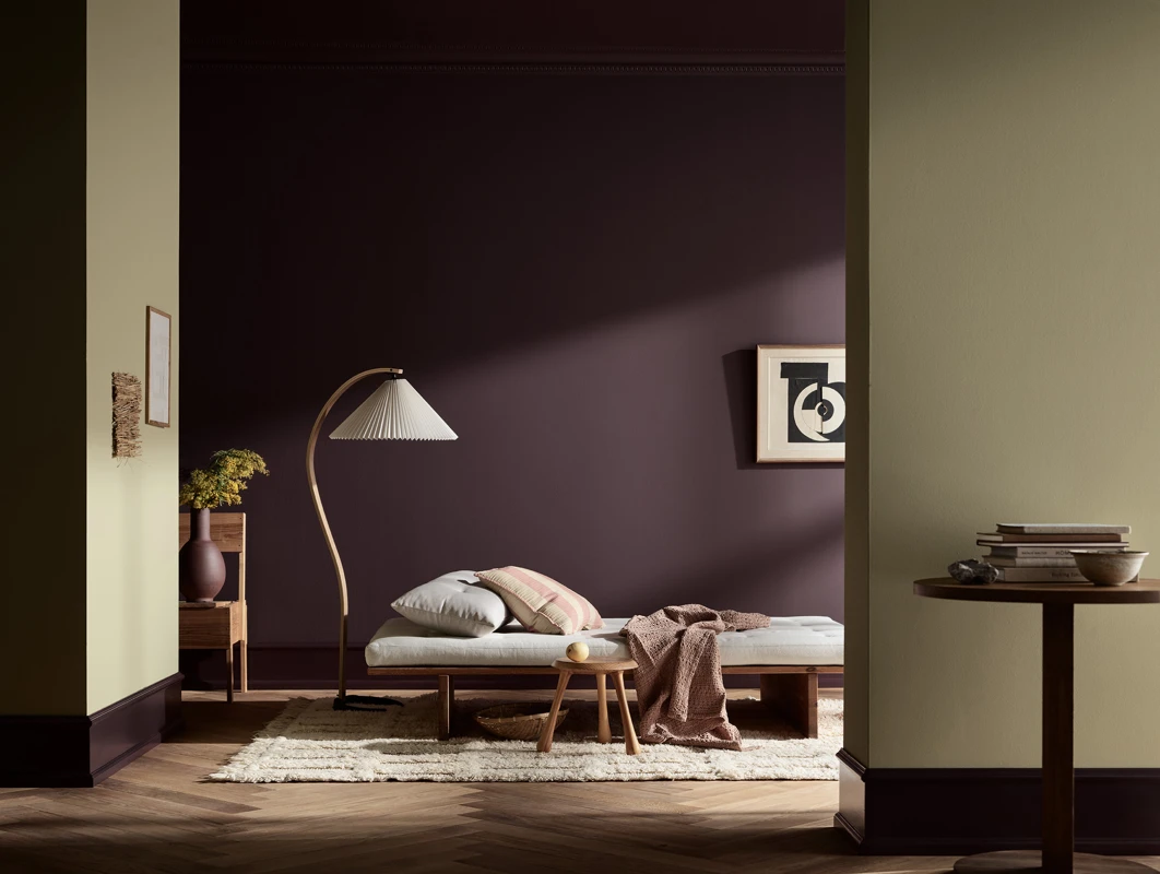 Moderne minimalistisk soverom med en lav daybed, buet gulvlampe, mørk plommefarget vegg i Jotun-fargen Velvet Plum, nattbord i tre og koselig nøytral innredning.