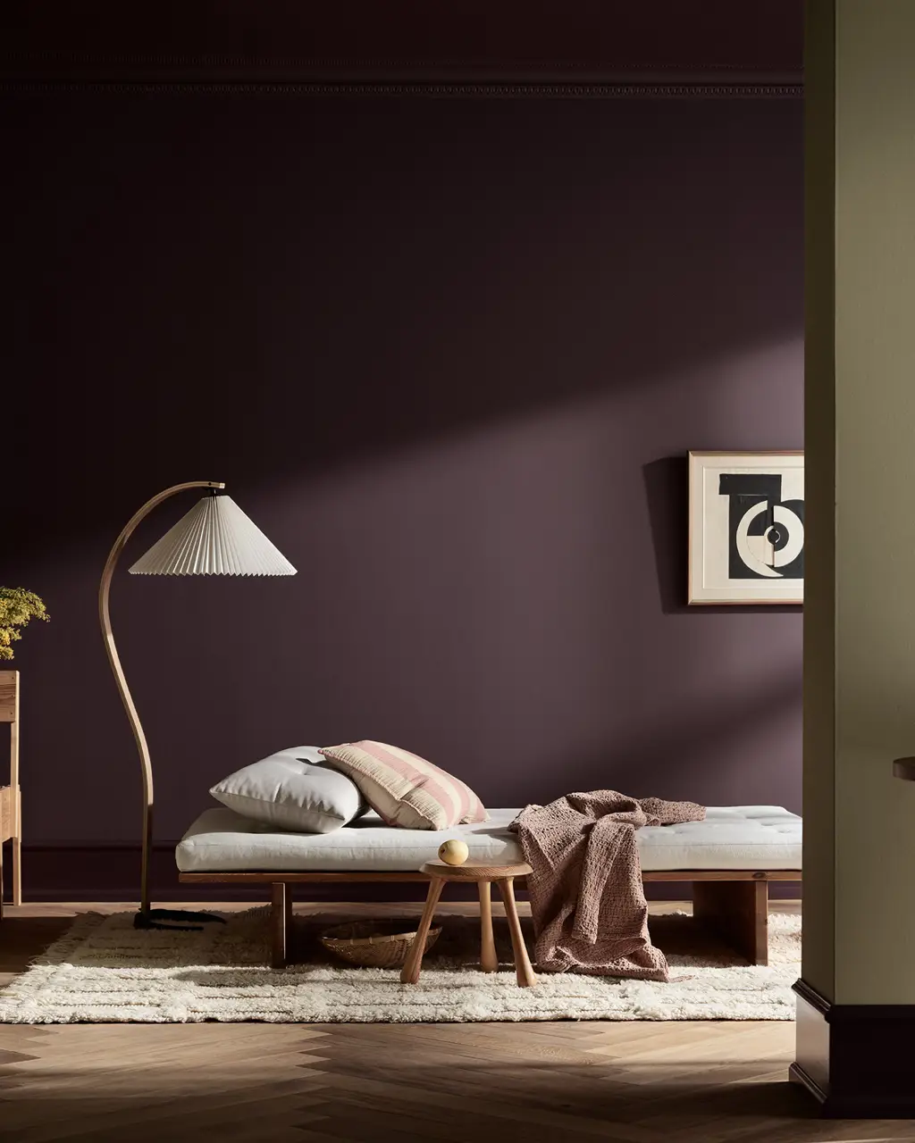 Moderne minimalistisk soverom med en lav daybed, buet gulvlampe, mørk plommefarget vegg i Jotun-fargen Velvet Plum, nattbord i tre og koselig nøytral innredning.