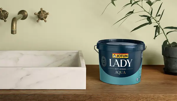 Jotun Lady Aqua vådrumsmaling i spand ved siden af en marmoreret vask på et træbord