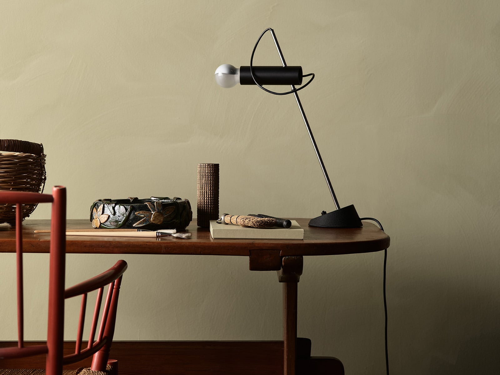 Stilrent skrivebord i tre med moderne bordlampe, dekorative gjenstander og rød stol i et minimalistisk interiør malt med kalkmaling LADY Minerals i fargen Biri