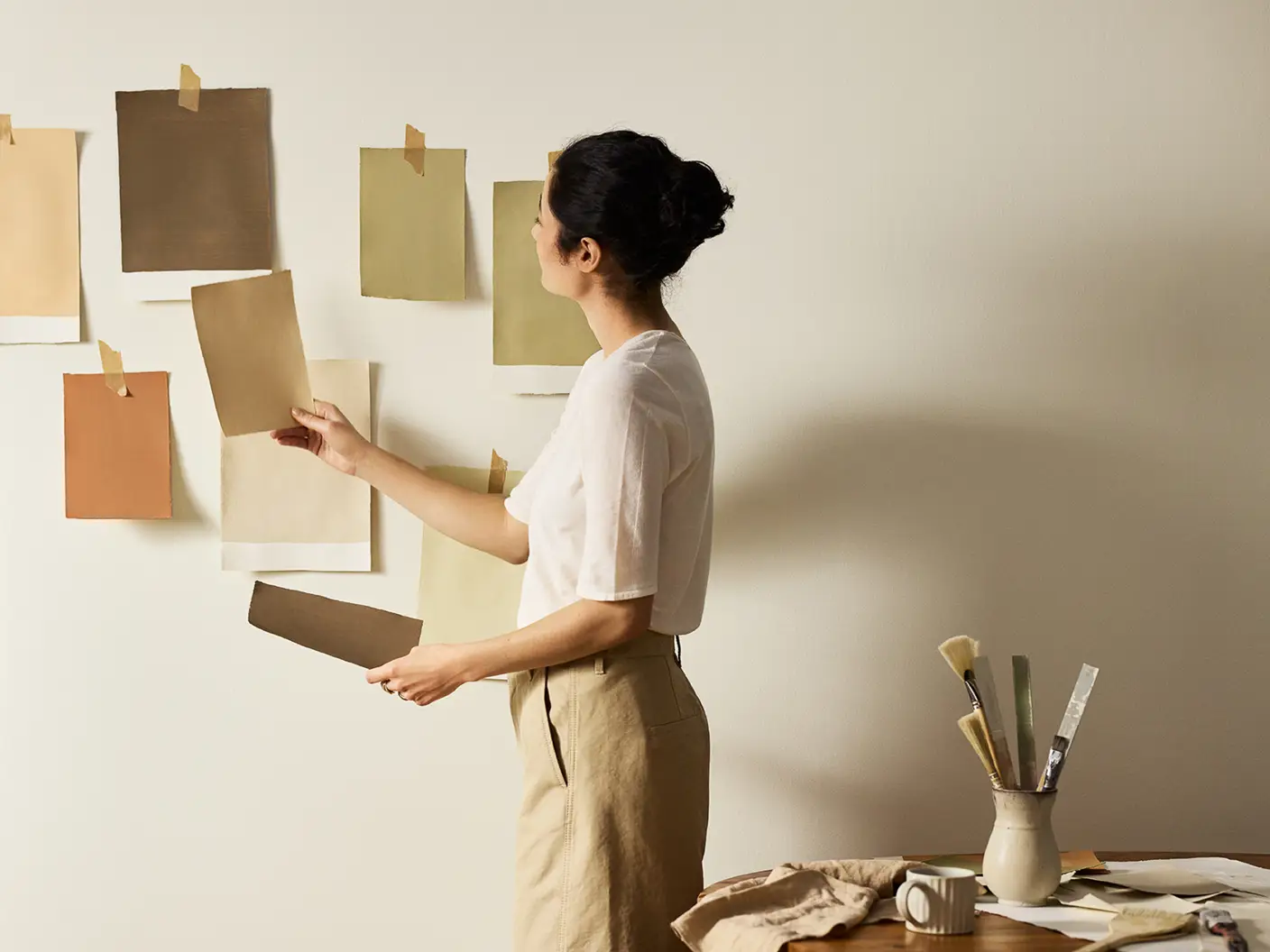 Kvinne henger opp fargeprøver malt med Jotun-farger på en beige vegg malt i Jotun Soul