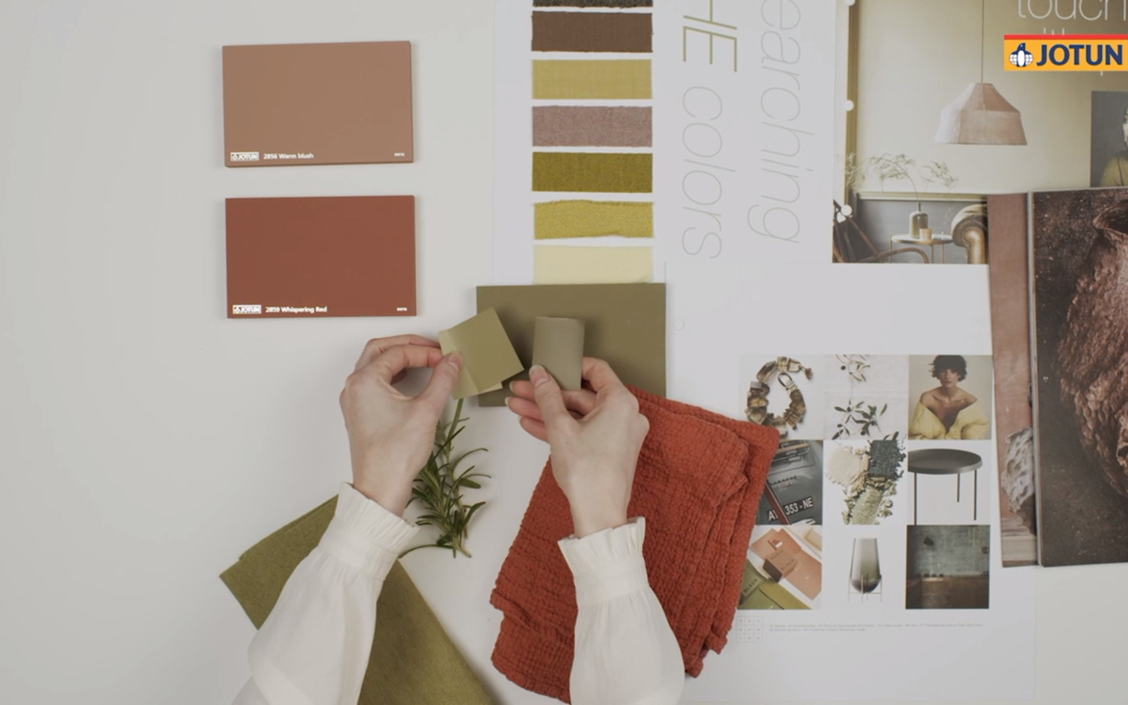 Two hands holding up colour samples towards a white wall, comparing the colours.