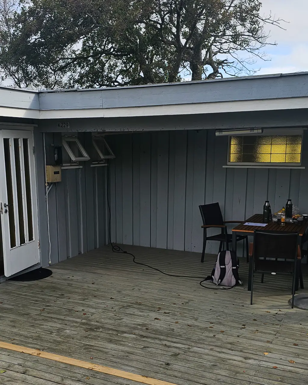 Hytteterrasse med overbygg før, grå terrasse og slitne blå vegger med et lite bord.