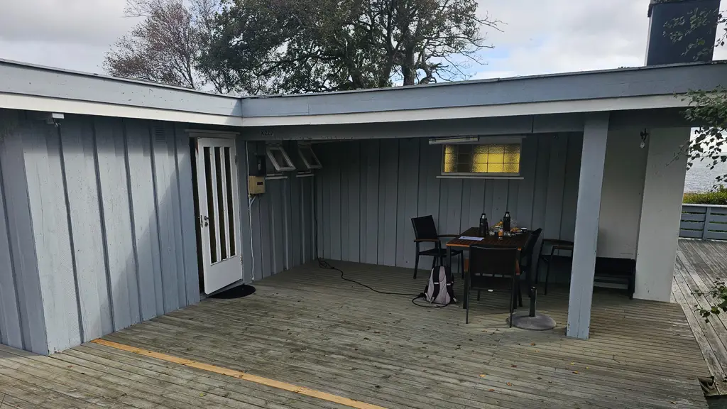 Hytteterrasse med overbygg før, grå terrasse og slitne blå vegger med et lite bord.