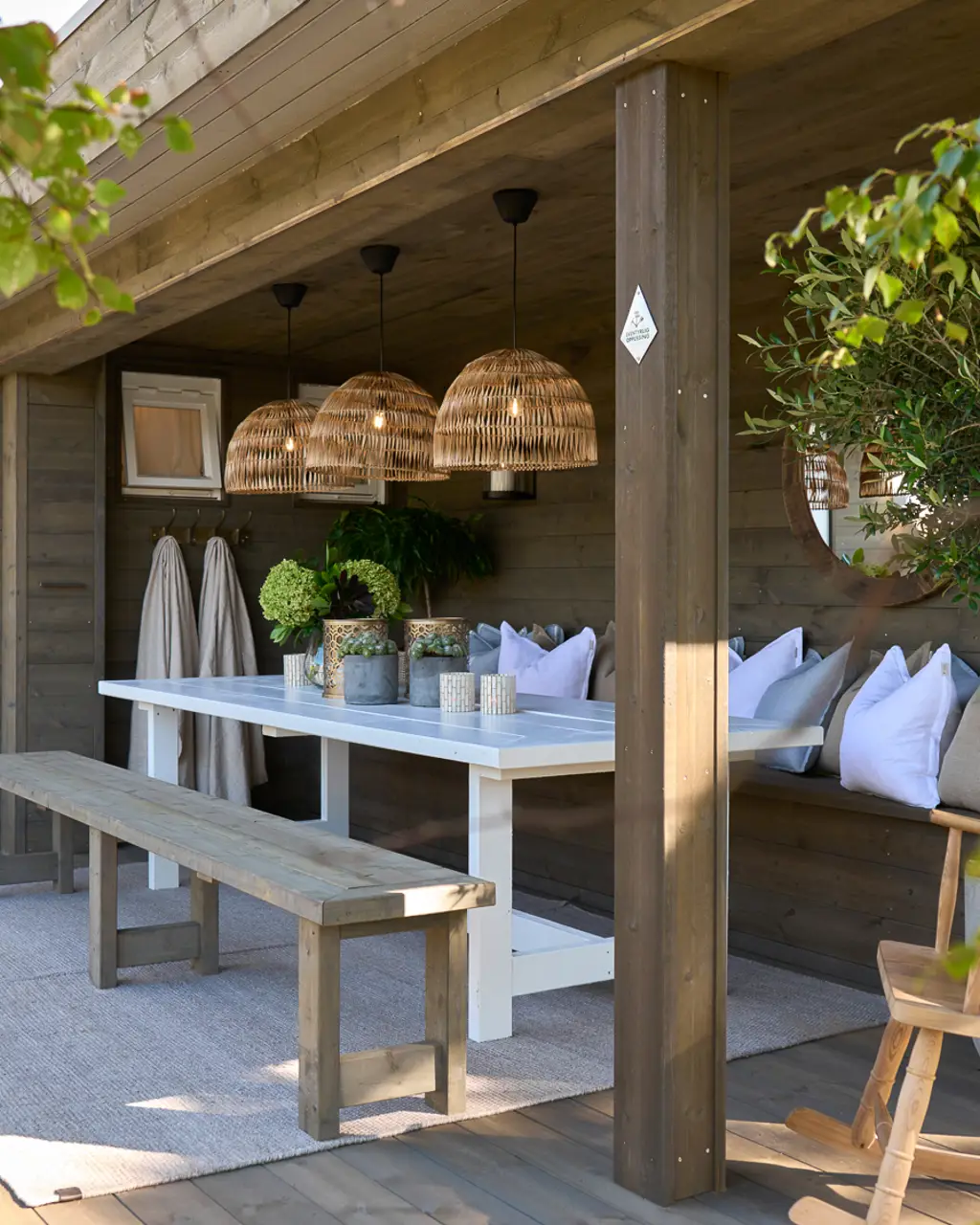 Hytteterrasse etter: med nytt terrassegulv, overbygg, benk med puter og stort bord med lamper over.