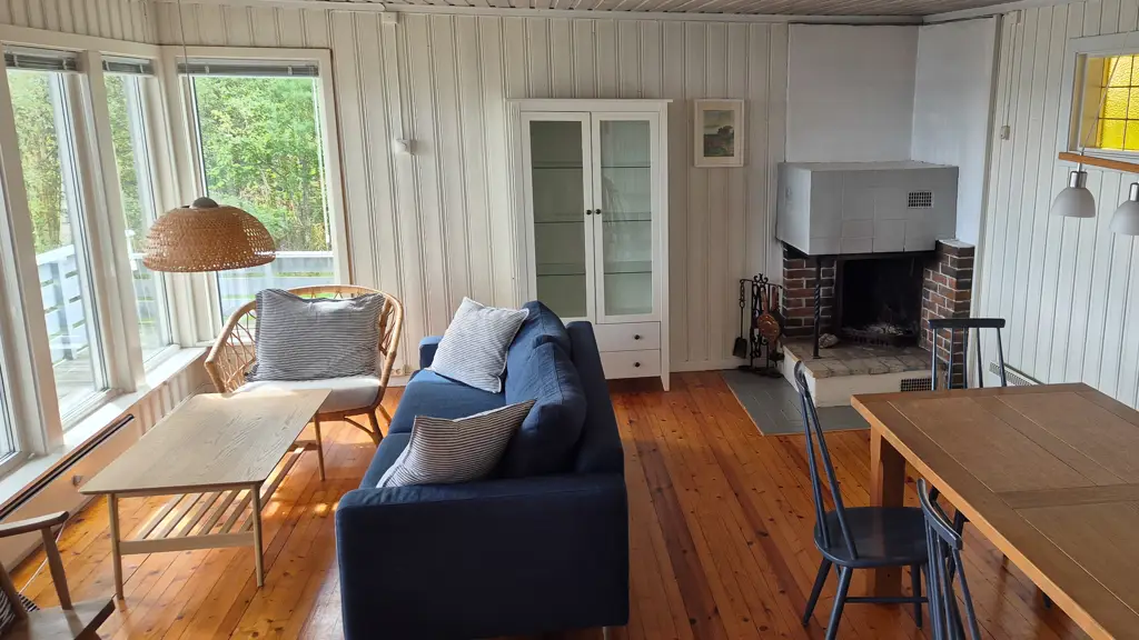 Stue på hytte i stavern før oppussing, slitte furugulv, panelvegger, blå sofa og stor peis