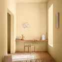 Minimalistisk hjemmekontor med lysgule vegger i fargen Jotun Cheerful Peach, skrivebord, stol, dekor og naturlig sollys.